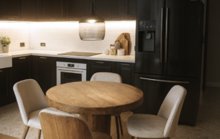 Nowoczesna kuchnia w jasnej, stonowanej kolorystyce. Na ścianie znajduje się zabudowa meblowa, a pod nią długi blat roboczy z wbudowanym zlewem i płytą grzewczą. Przestrzeń jest minimalistyczna, uporządkowana i zaprojektowana w eleganckim, funkcjonalnym stylu.